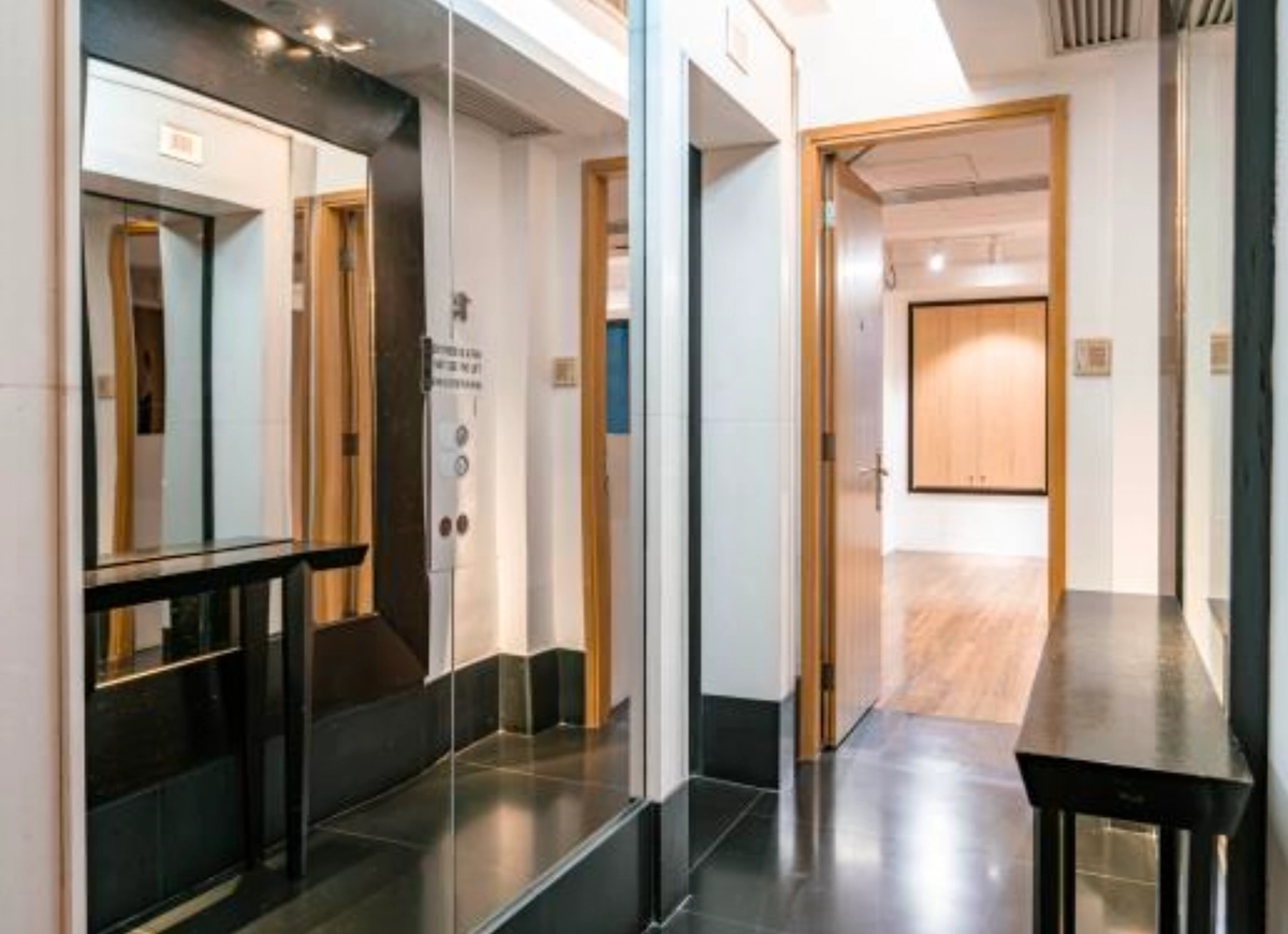 A hallway in Central with mirrors, black tables, open doors, and white walls leading to a room with wooden paneling.