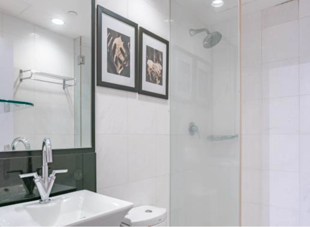 Bathroom on D’Aguilar Street, Central with white sink, glass shower, wall art, towel rack, and tiled walls.