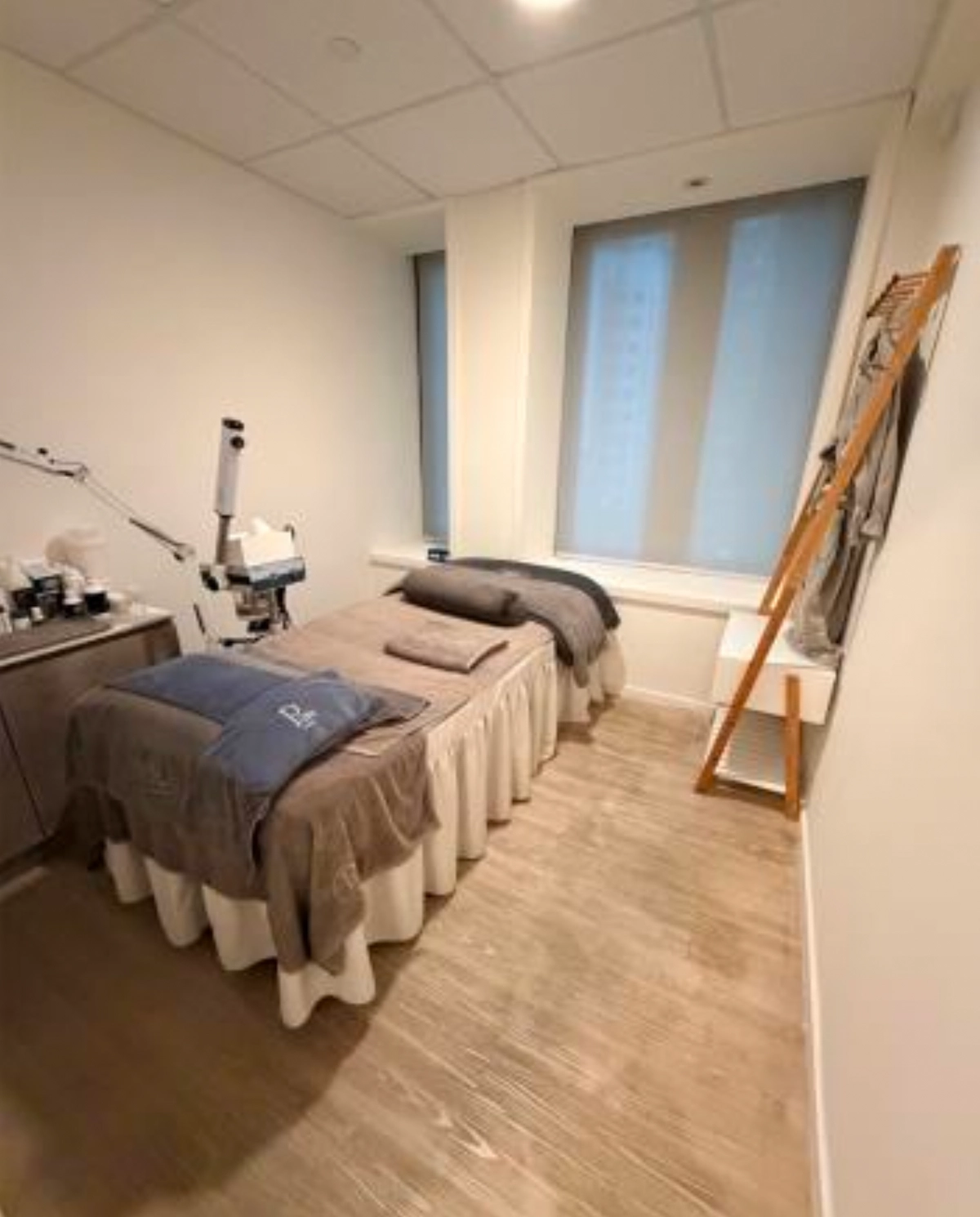 Treatment room in Central on D’Aguilar Street with a single bed, folded towels, a lamp and neutral-toned décor.