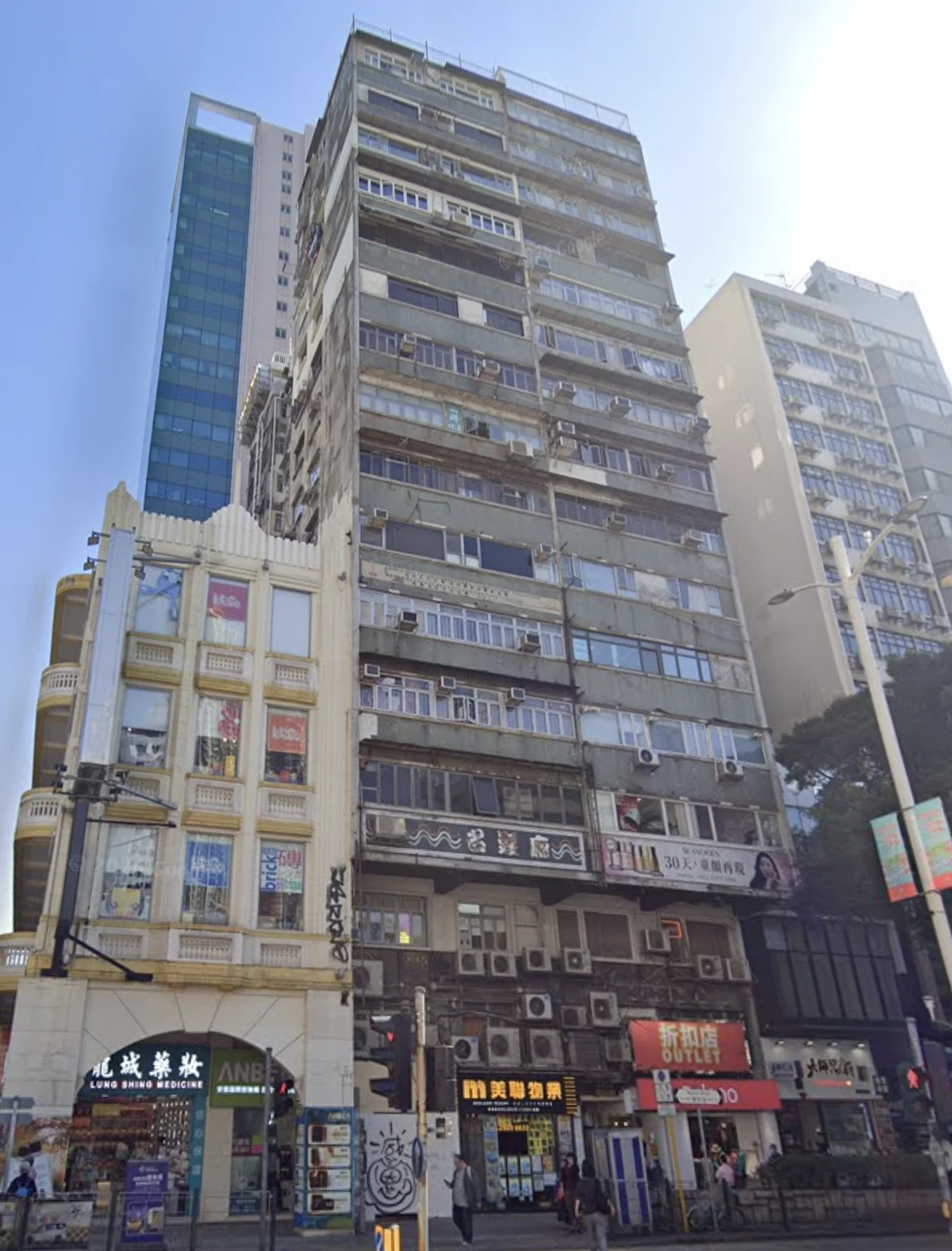 Older tall apartment building with balconies and air conditioners on Nathan Road, among shops and busy city surroundings.