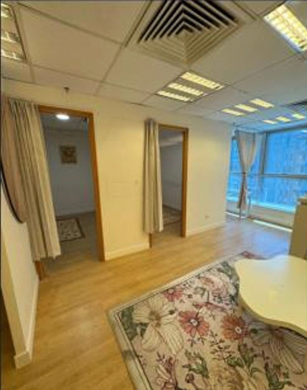 Office space on Granville Road featuring wood flooring, two doorways, a large window, white walls, and a floral rug.
