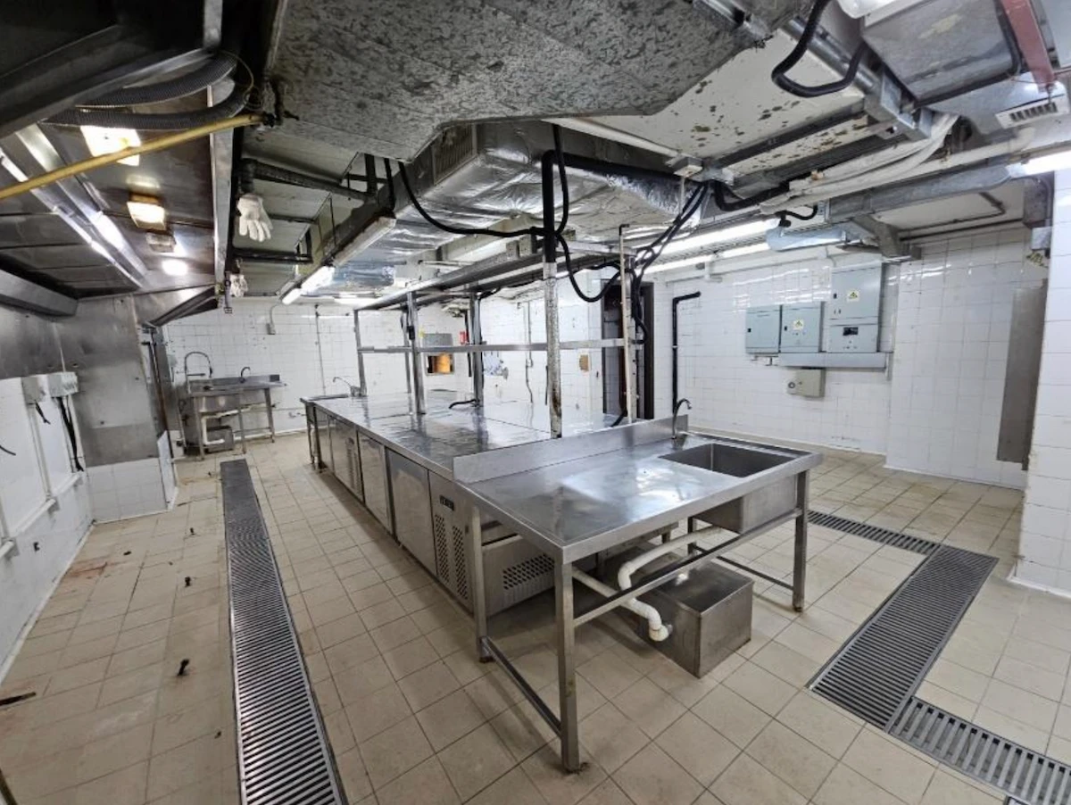 Large empty industrial kitchen on Granville Road Tsim Sha Tsui with metal counters sinks and exposed pipes.