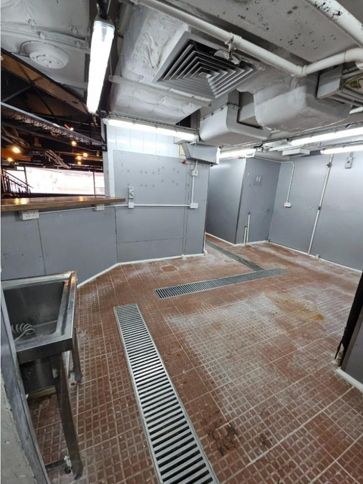 Industrial room on Granville Road, Tsim Sha Tsui with tiled floor, drains, metal sink, gray walls and exposed pipes.