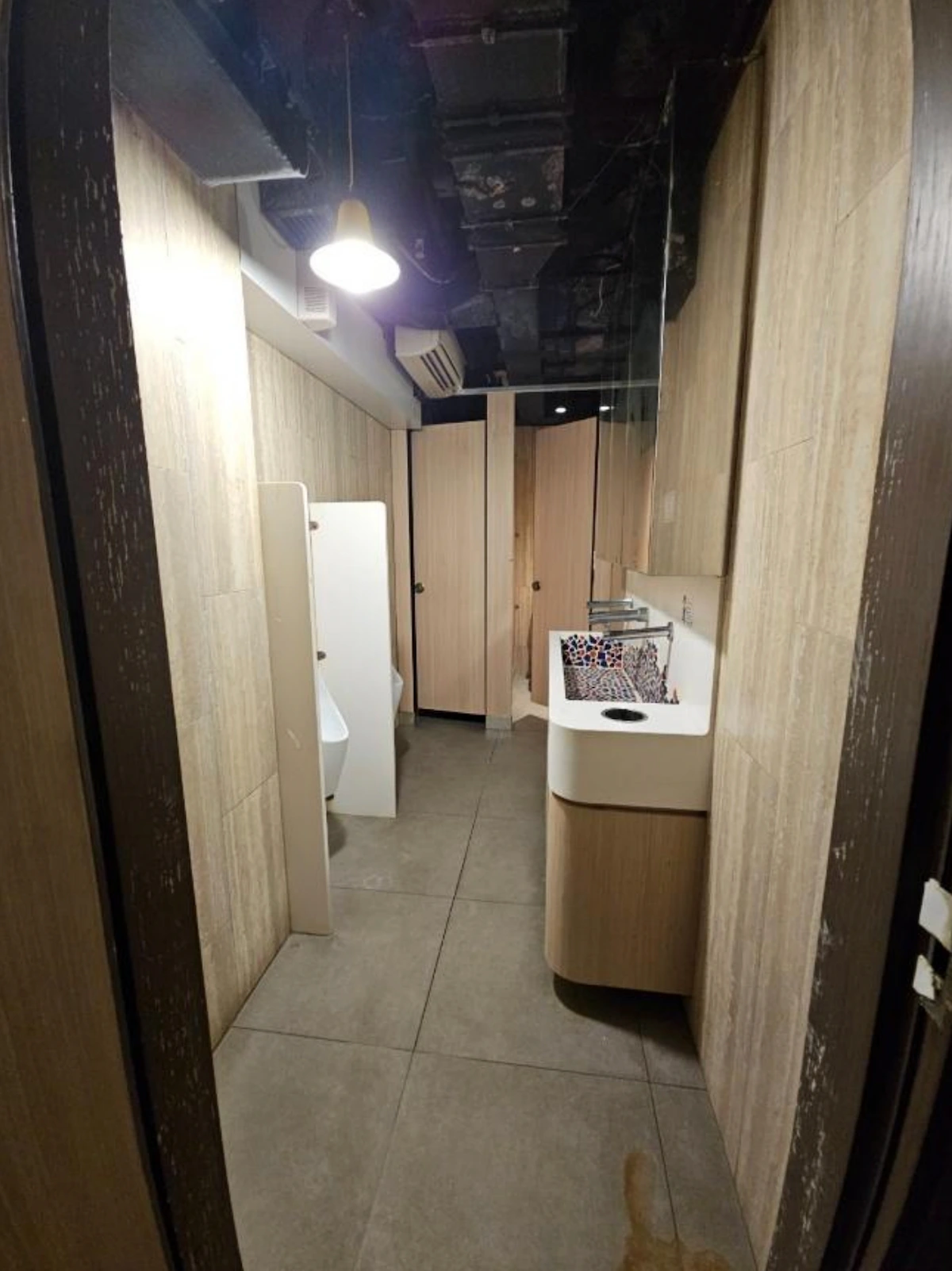 Public restroom on Granville Road, Tsim Sha Tsui with tiled walls, urinal, sink, mirror, stall and exposed pipes.