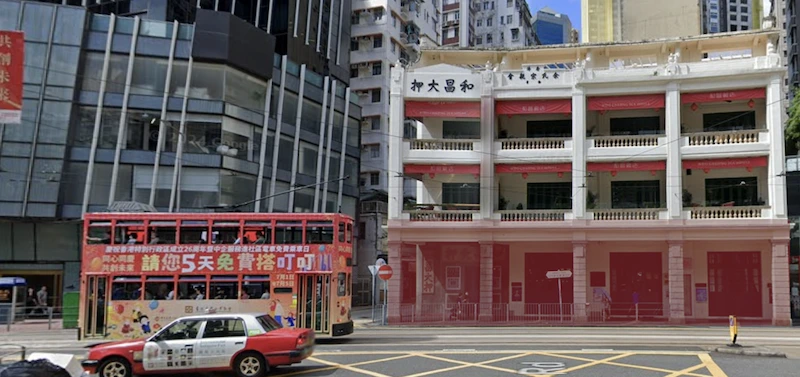 Restaurant space on Ship Street, Wan Chai. A red tram and a taxi drive past modern glass and white buildings, Hong Kong.