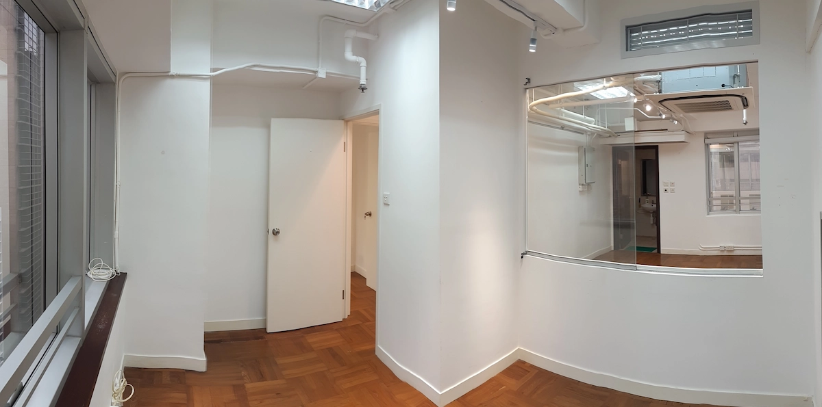 Empty room with white walls, wood floor, large mirror, and windows on the left near Queen’s Road Central.