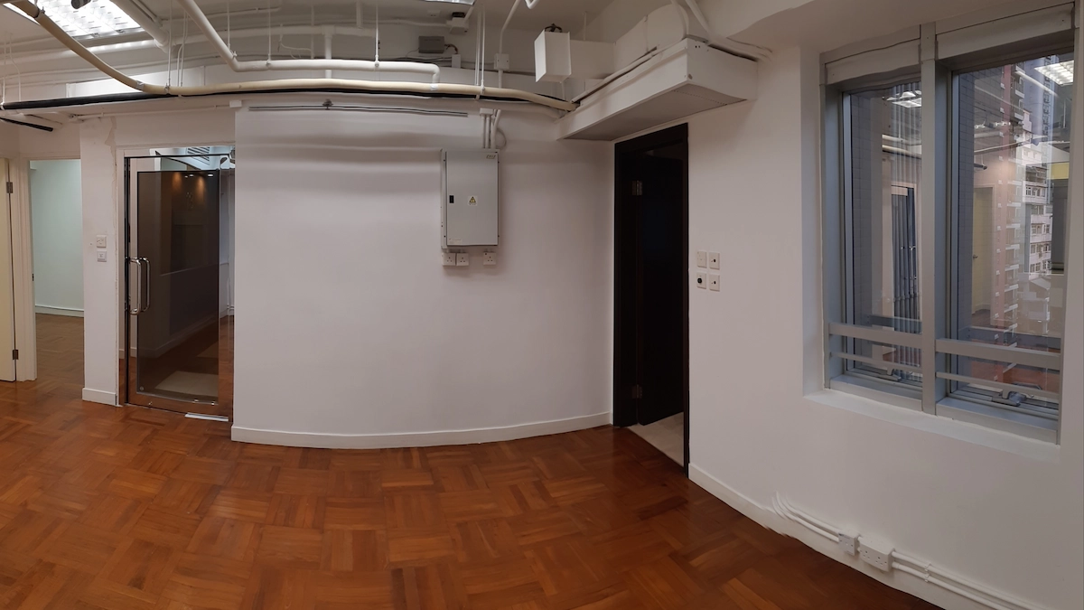 Office space on Queen’s Road Central with wood flooring, glass door, white walls, exposed pipes and window on the right.