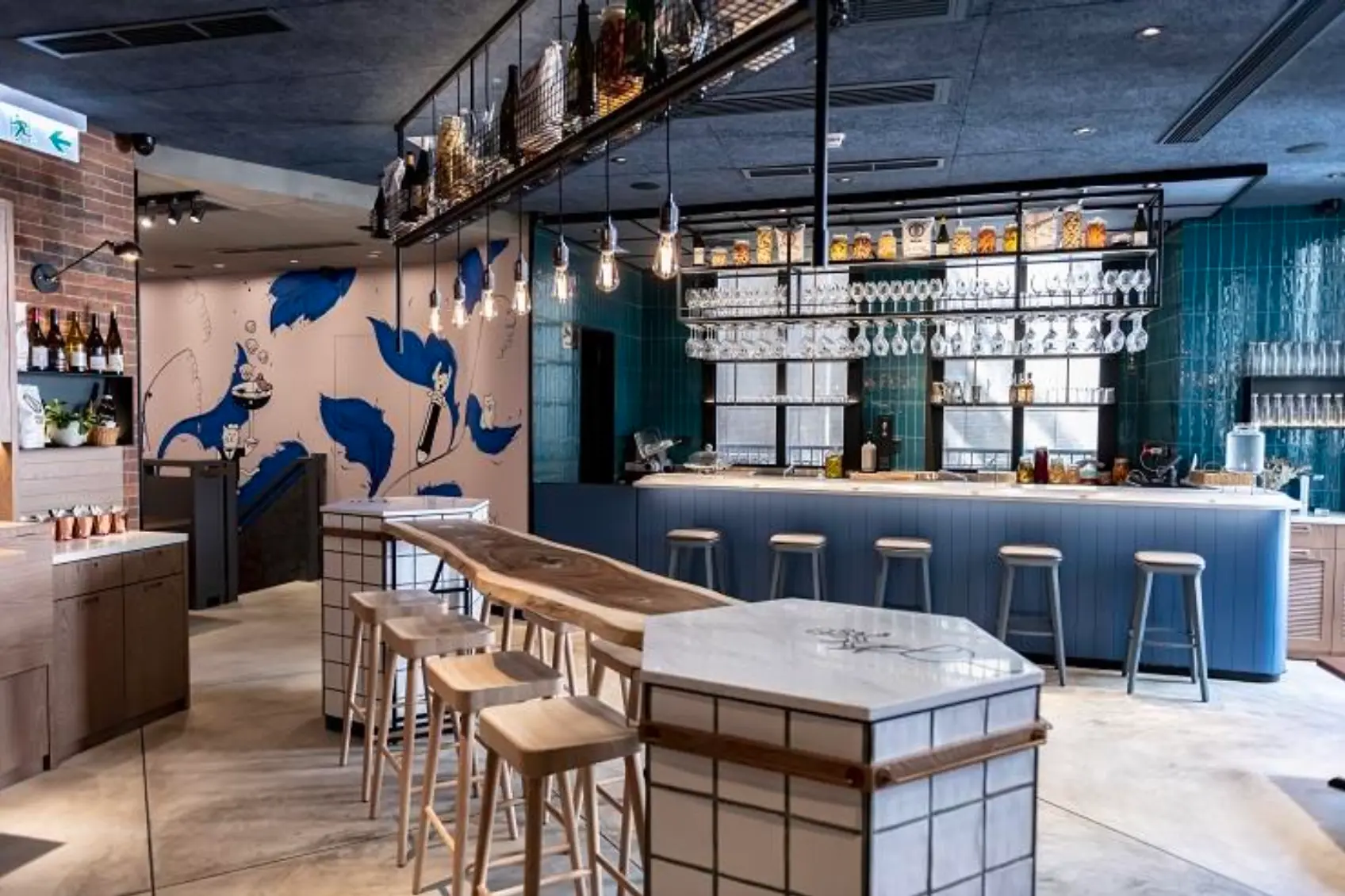 Bar on Lee Tung Avenue with high stools, a blue mural wall, and exposed pipes in a brightly lit Wan Chai setting.