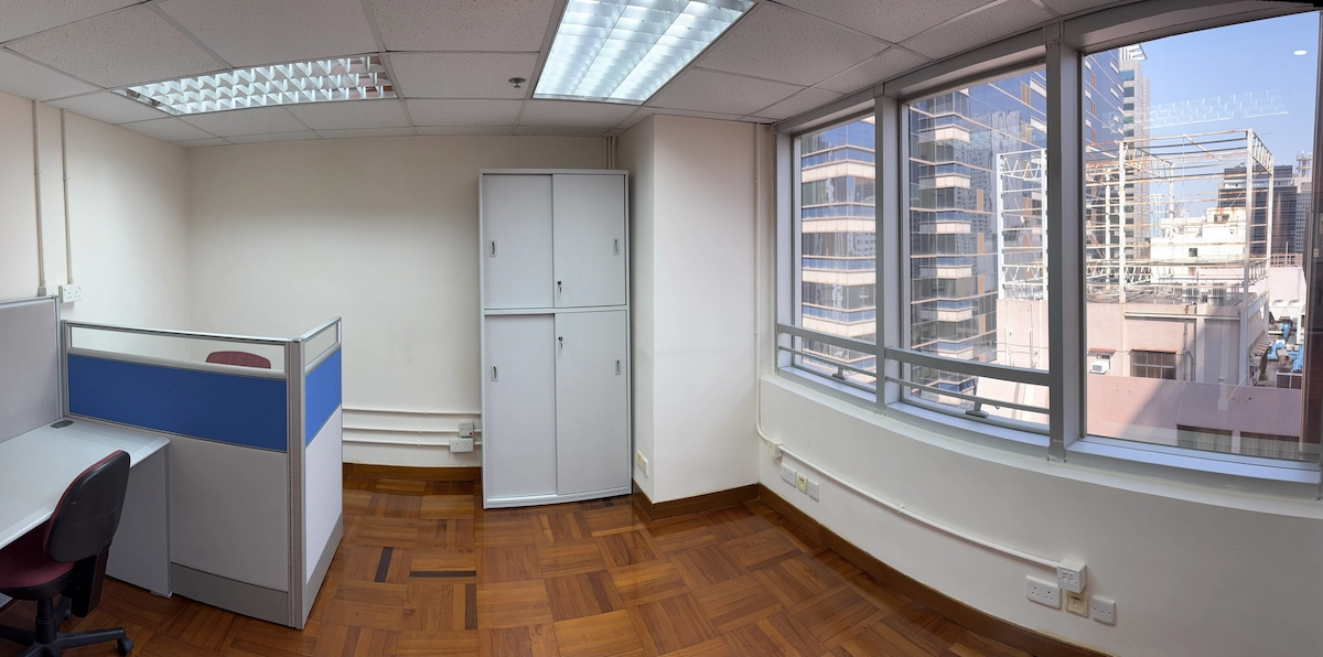 Small office with cubicle, storage cabinets, and wood floor overlooks Queen’s Road Central and tall city buildings.