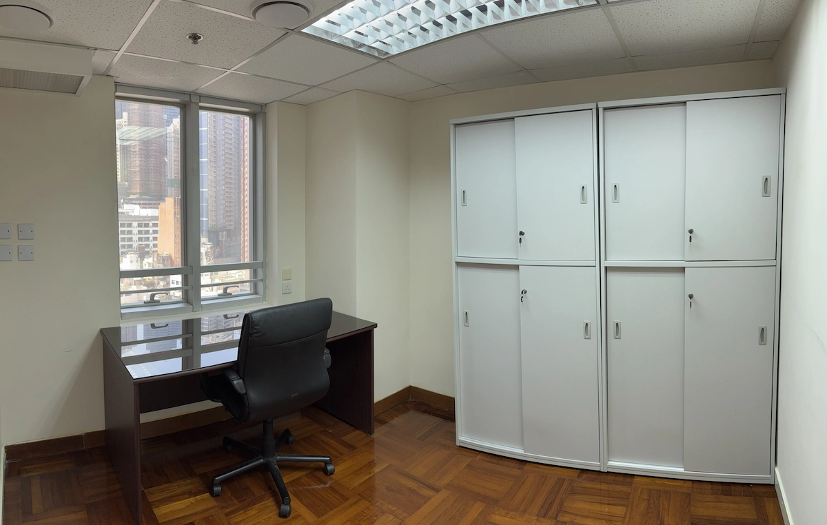 Small office in Central with a desk, black chair, city view through window, and two white storage cabinets by the wall.