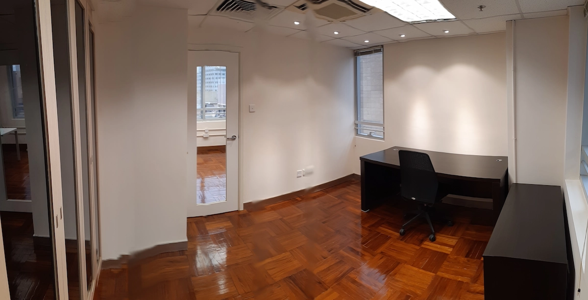 Empty office in Central with a black desk and chair, wooden floor, white walls, and large windows letting in natural light.