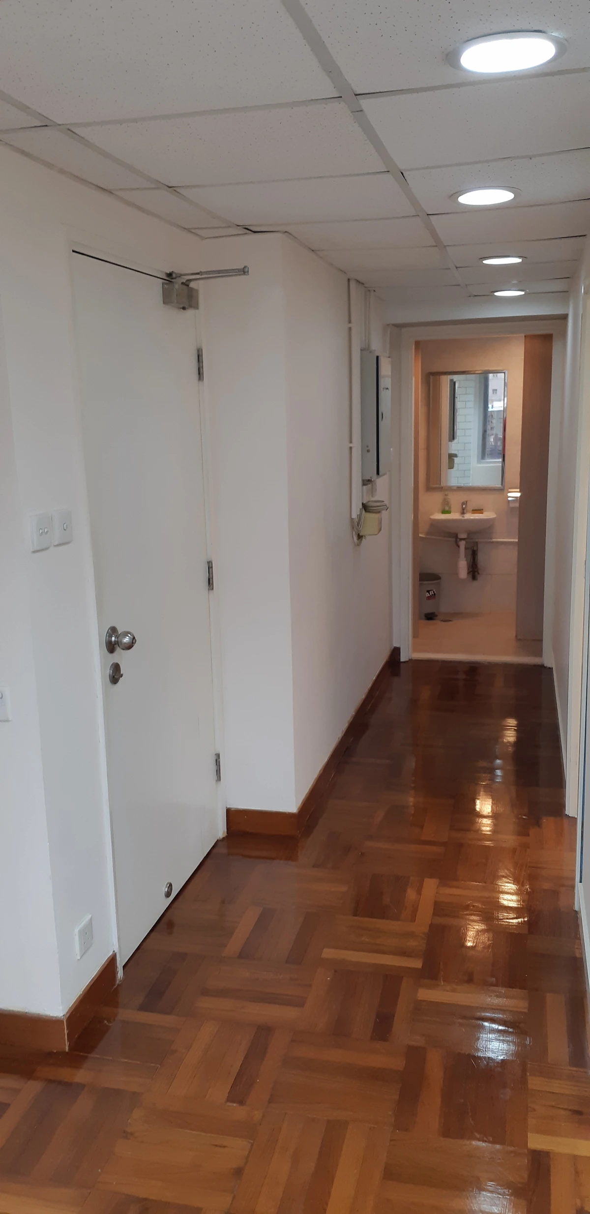 Hallway with wooden floors and white walls, doors on both sides, leading to a bathroom in classic Central style.