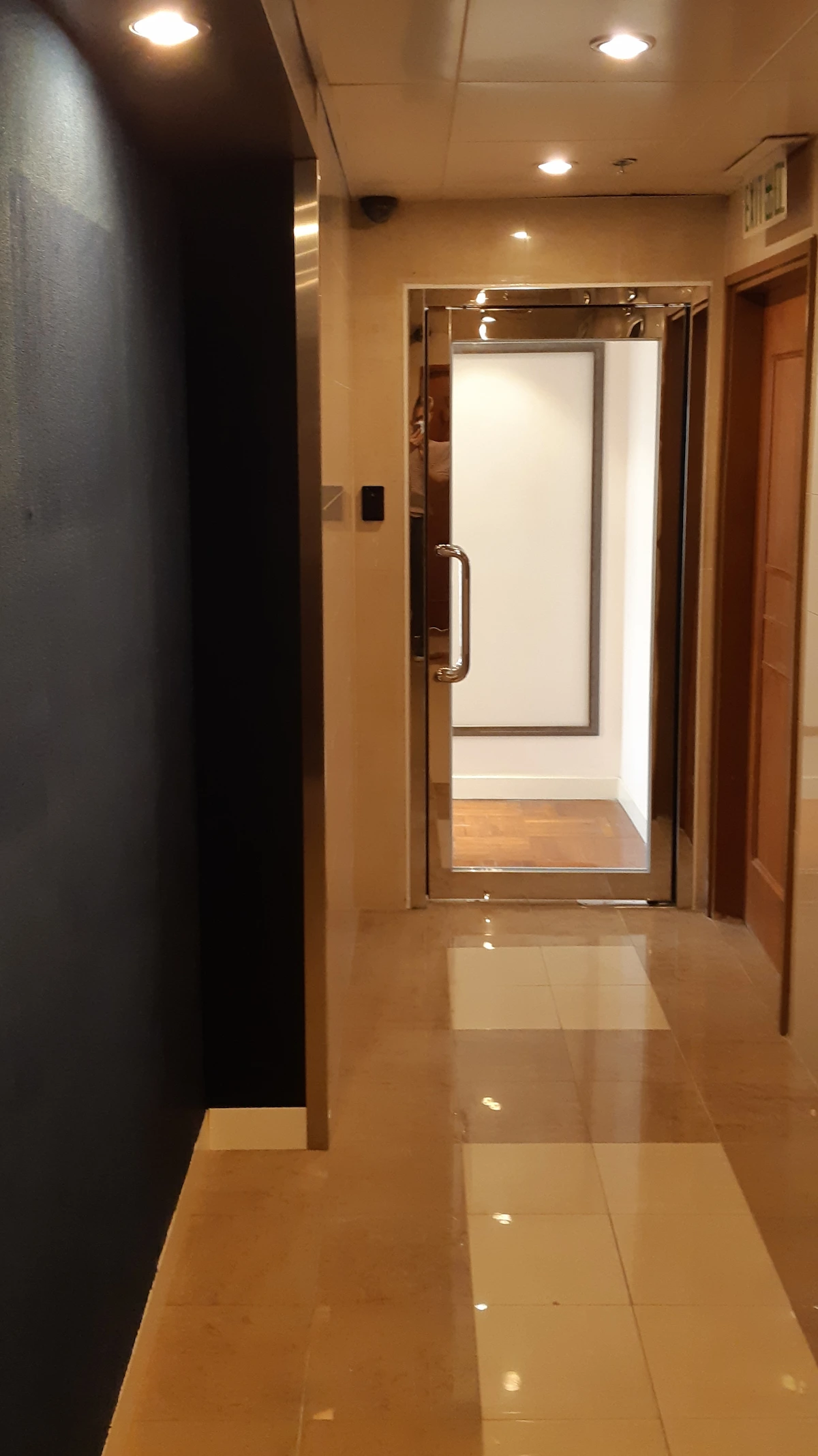 A beige tiled hallway near Queen’s Road Central ends at an open glass door that leads into a brightly lit white-walled room.