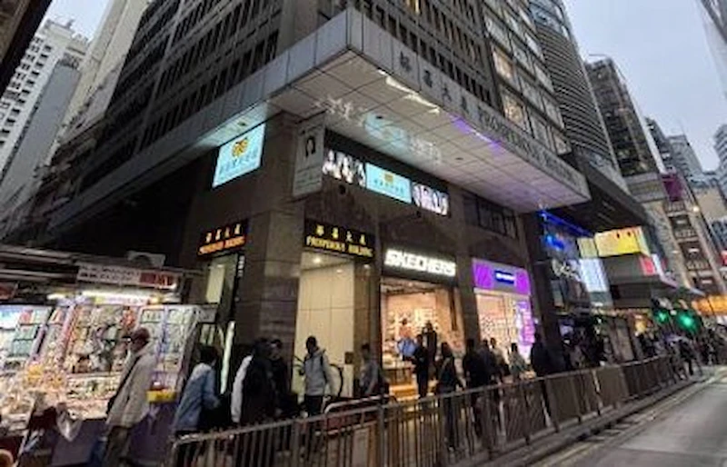 Shop on Des Voeux Road Central, Central. People walk past shops, including a Skechers store, at the base of a tall city building.