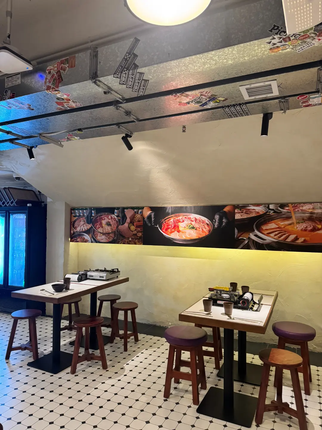 Restaurant interior on Hollywood Road, Central, with tables, stools, dishware, food photos, and a sticker-covered vent.