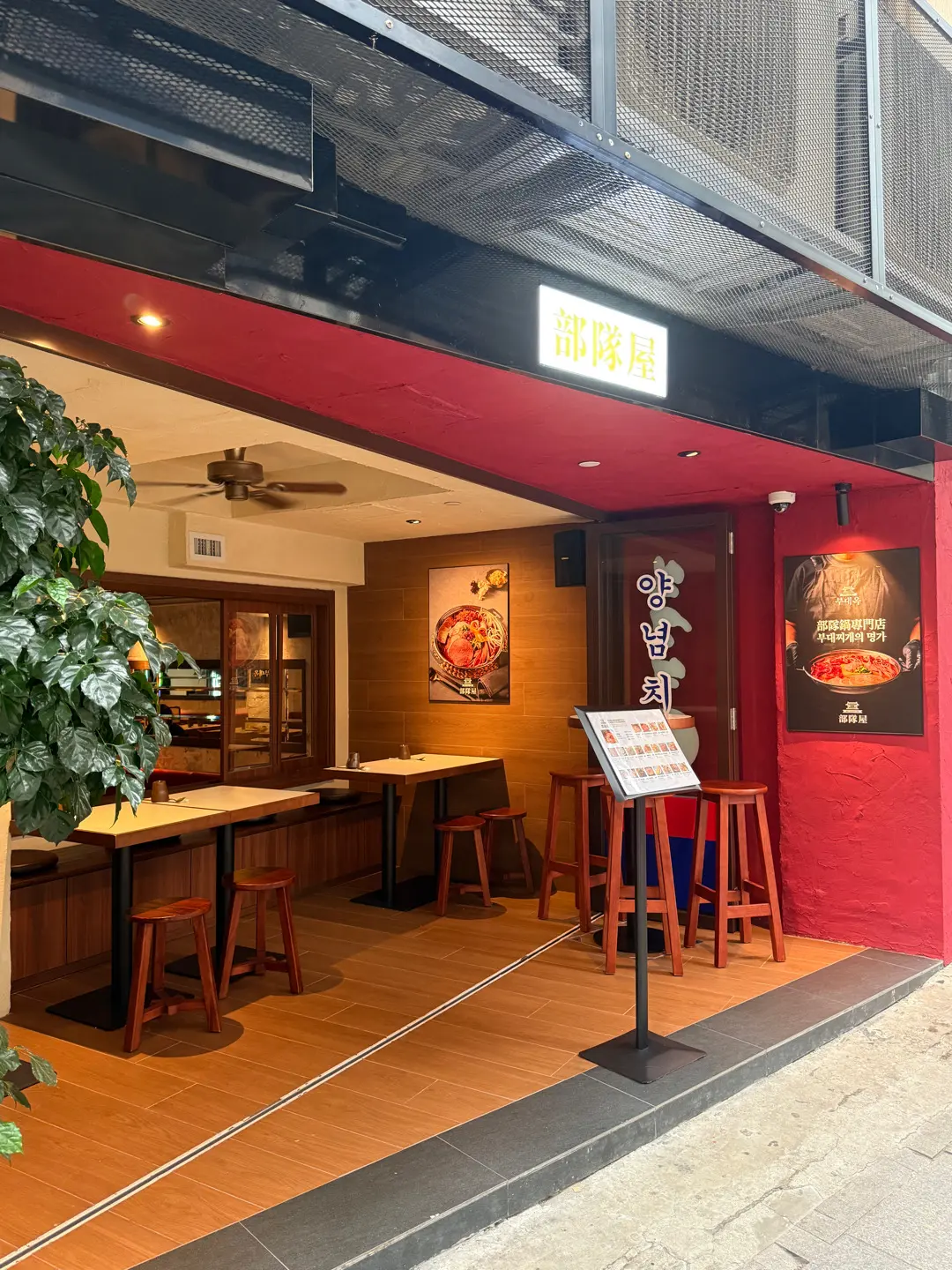 Red-fronted restaurant on Hollywood Road with wooden tables, plant near entrance, and food posters visible inside.