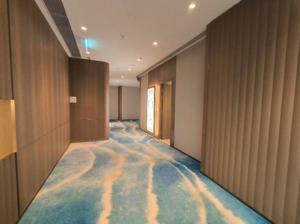 Hallway on Mody Road featuring wood-paneled walls, blue wave-patterned carpet, and ceiling lights.