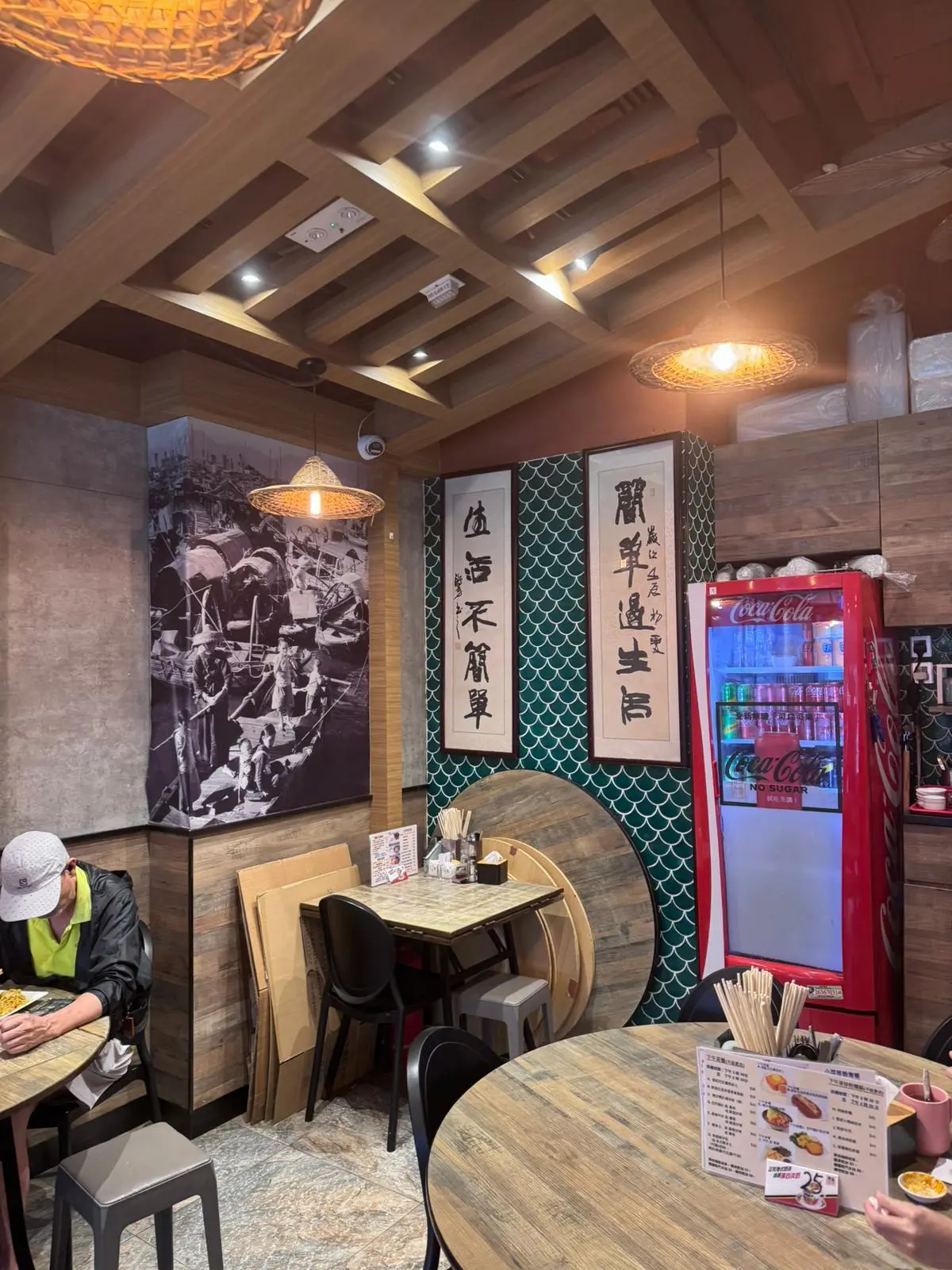 Small restaurant on Ap Lei Chau Main Street with round tables, Coca-Cola fridge, wall art, and one person seated on the left.