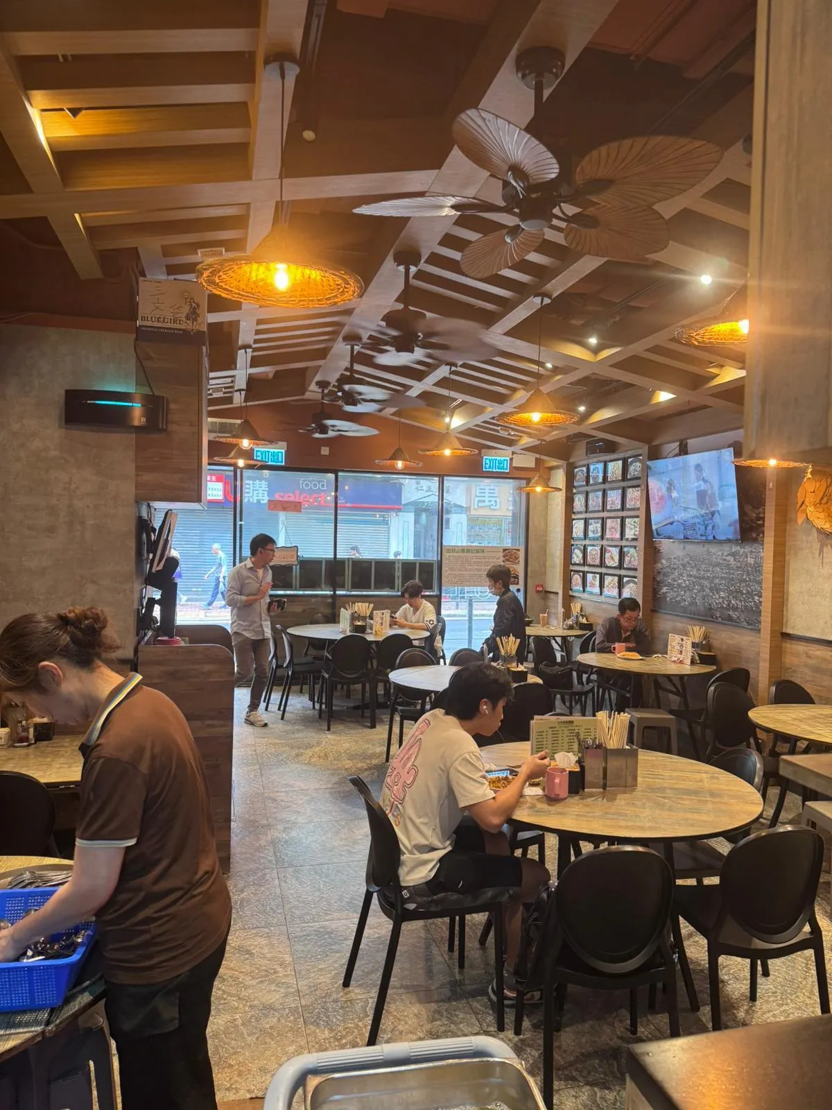 Several people are dining in a well-lit restaurant on Ap Lei Chau Main Street with wooden decor and staff near the entrance.