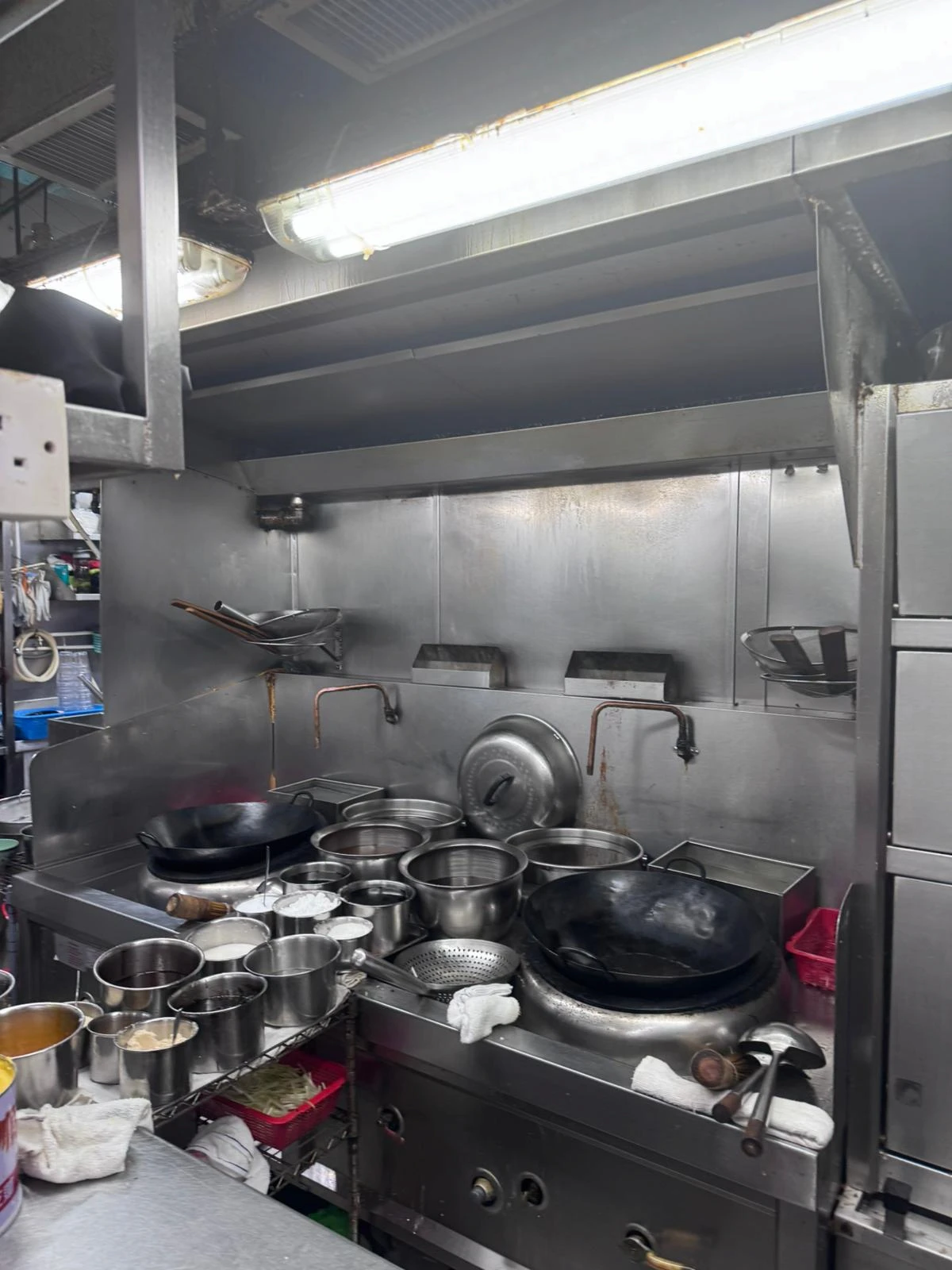 A commercial kitchen on Ap Lei Chau Main Street has metal pots woks and stainless steel surfaces under fluorescent lights.