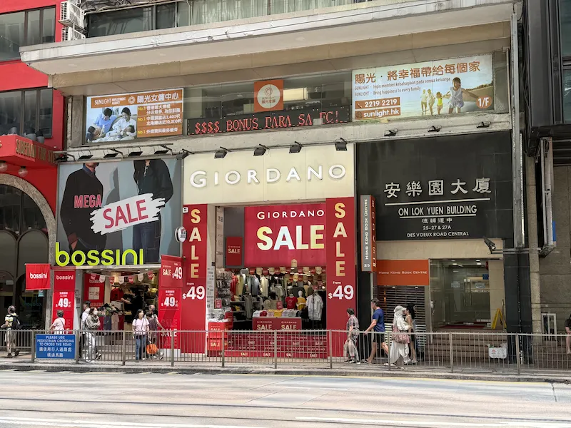 Shop on Des Voeux Road Central, Central. Street view of Giordano store with mannequins in the window and people passing by.