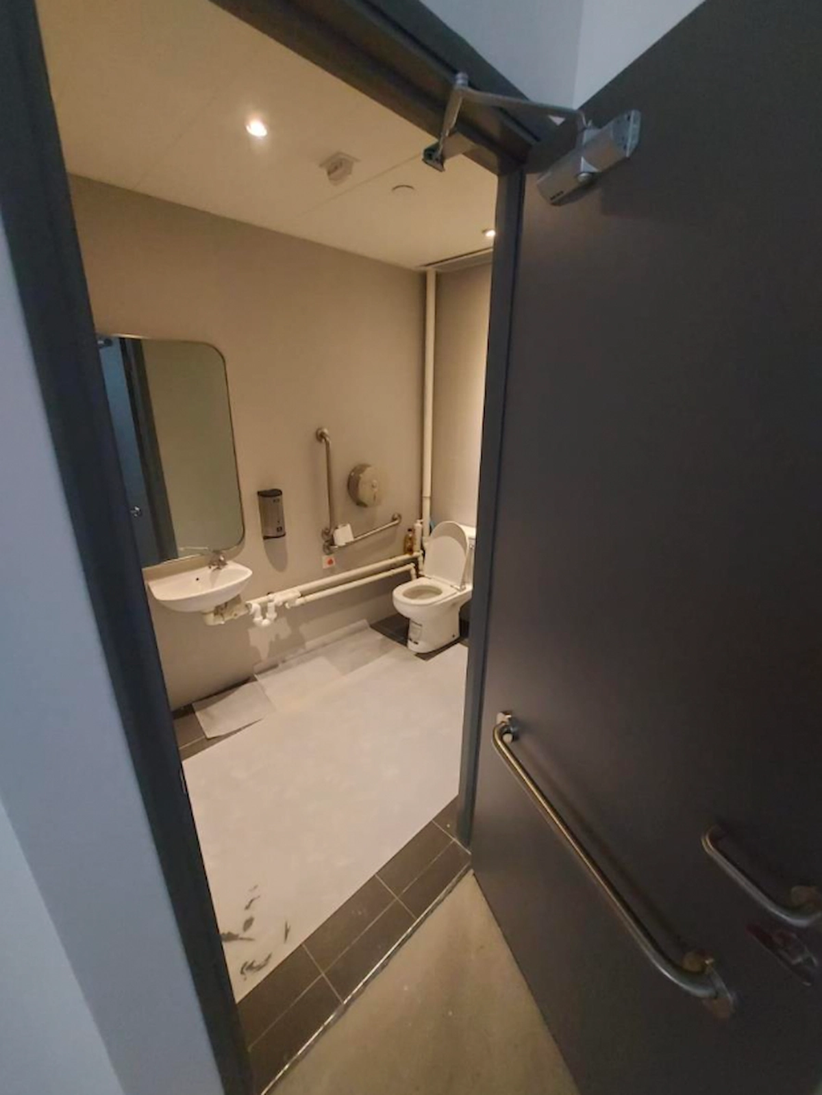 Accessible bathroom off Wellington Street with toilet, grab bars, sink, mirror, and soap dispenser.