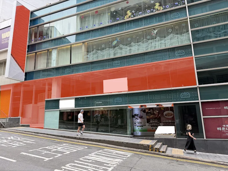 Restaurant space on Wellington Street, Central. A man and a woman walk past a modern glass building on sloped Wellington Street.