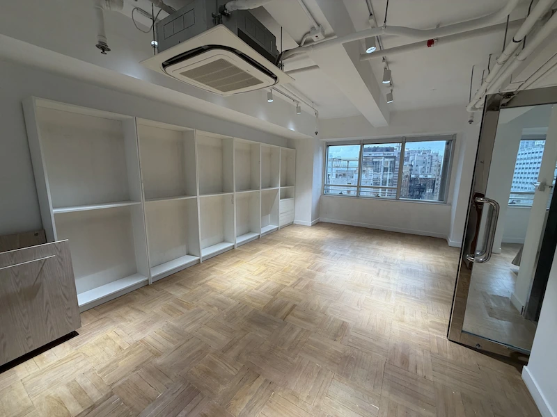 Office on Queen's Road Central, Central. Empty room with wooden floor, white built-in shelves, and a large window near Queen’s Road Central.