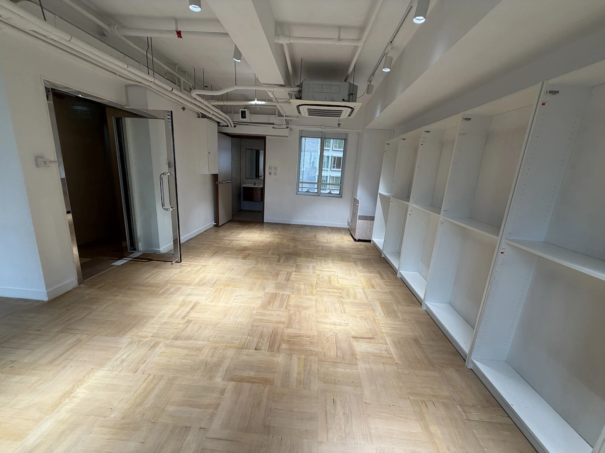 Empty room on Queen’s Road Central with wooden floors, white shelves, glass doors, and natural light.