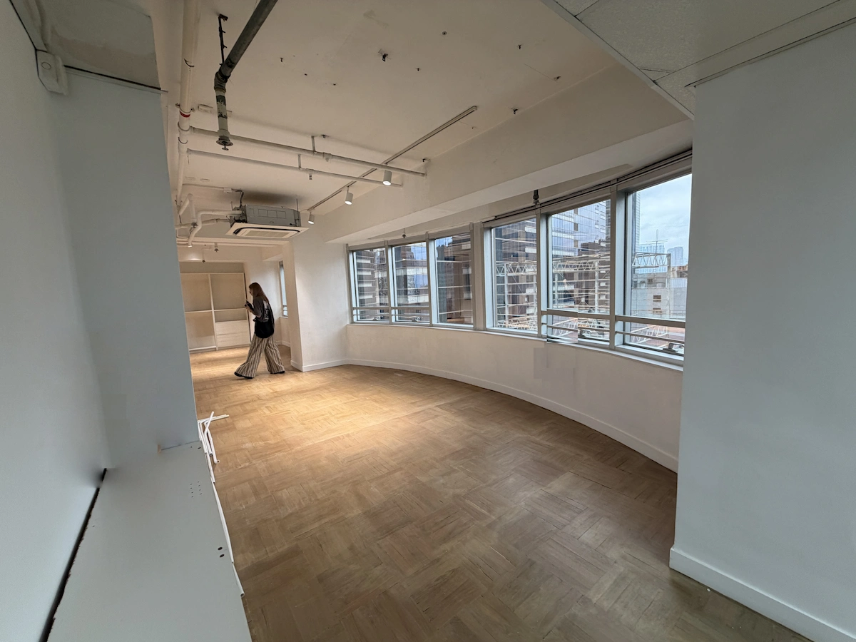 A person stands near windows in an empty, curved Central office space with wood floors and views of the city.
