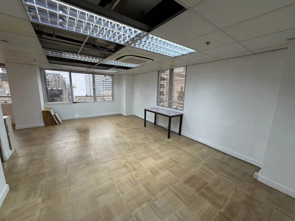 Empty office in Central with wood floors, large windows, and a table near the window overlooking Queen’s Road Central.