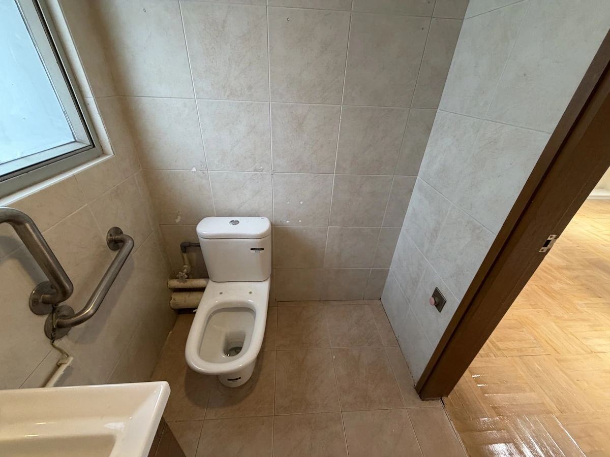 Compact Central bathroom with toilet, grab bar, sink, tiled walls, and a wooden door open to another floor.