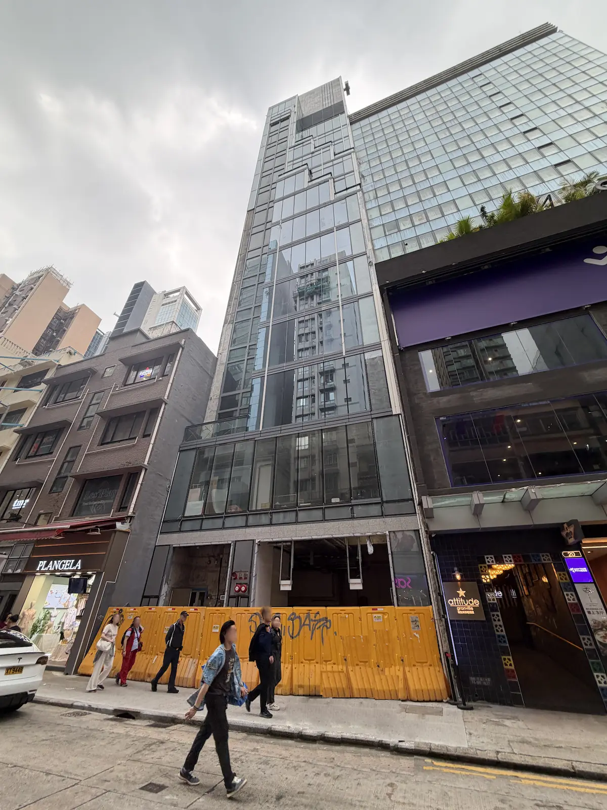 尖沙咀加連威老道一幢現代玻璃大廈地下設舖位，有人步行，天空多雲。