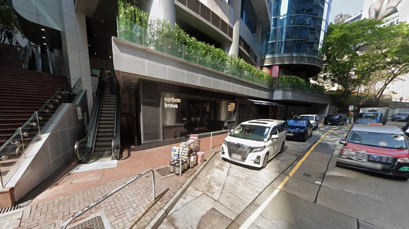 Street view of Carbon Brews bar on Wyndham Street, Central, with cars parked by an escalator and glass-fronted buildings.