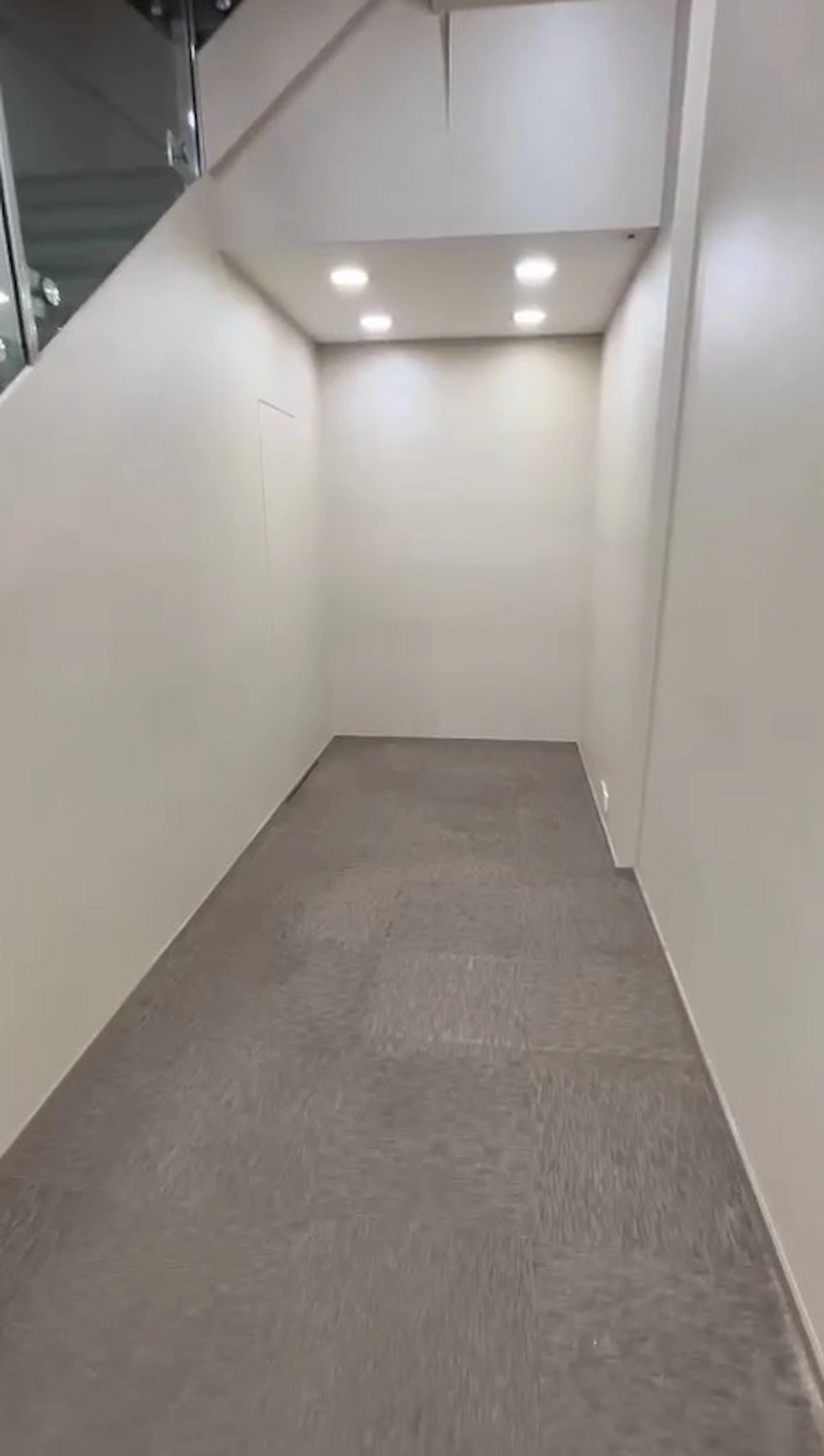A narrow, empty hallway with gray carpet and white walls resembling a corridor near Lan Fong Road in Causeway Bay.
