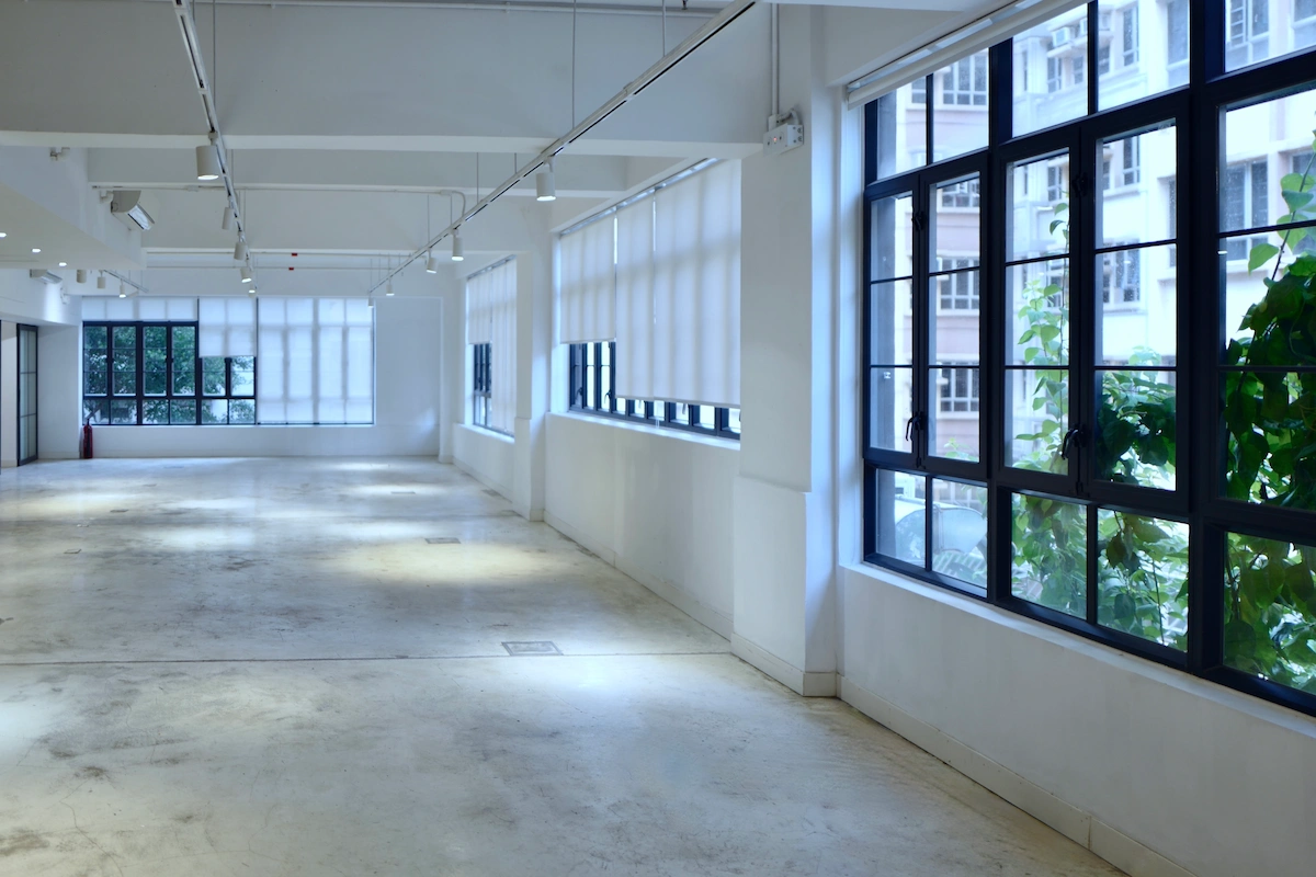 Empty room in Po Hing Fong, Sheung Wan with white walls, concrete floor, large windows and green plants visible outside.
