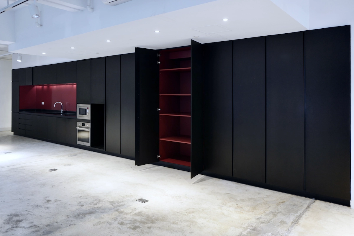 Sheung Wan kitchen featuring black cabinets, red backsplash, open pantry, built-in oven and concrete floor.