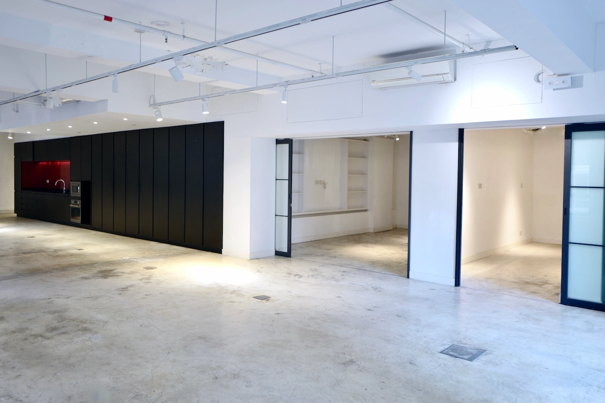 Room in Sheung Wan with white walls, concrete floor, black cabinets, and a kitchen area with a red backsplash.