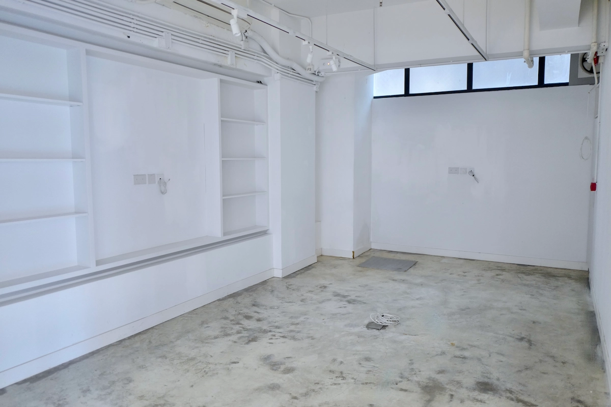 White minimalist room in Po Hing Fong, Sheung Wan with concrete floor, built-in shelves, high windows, and exposed outlets.