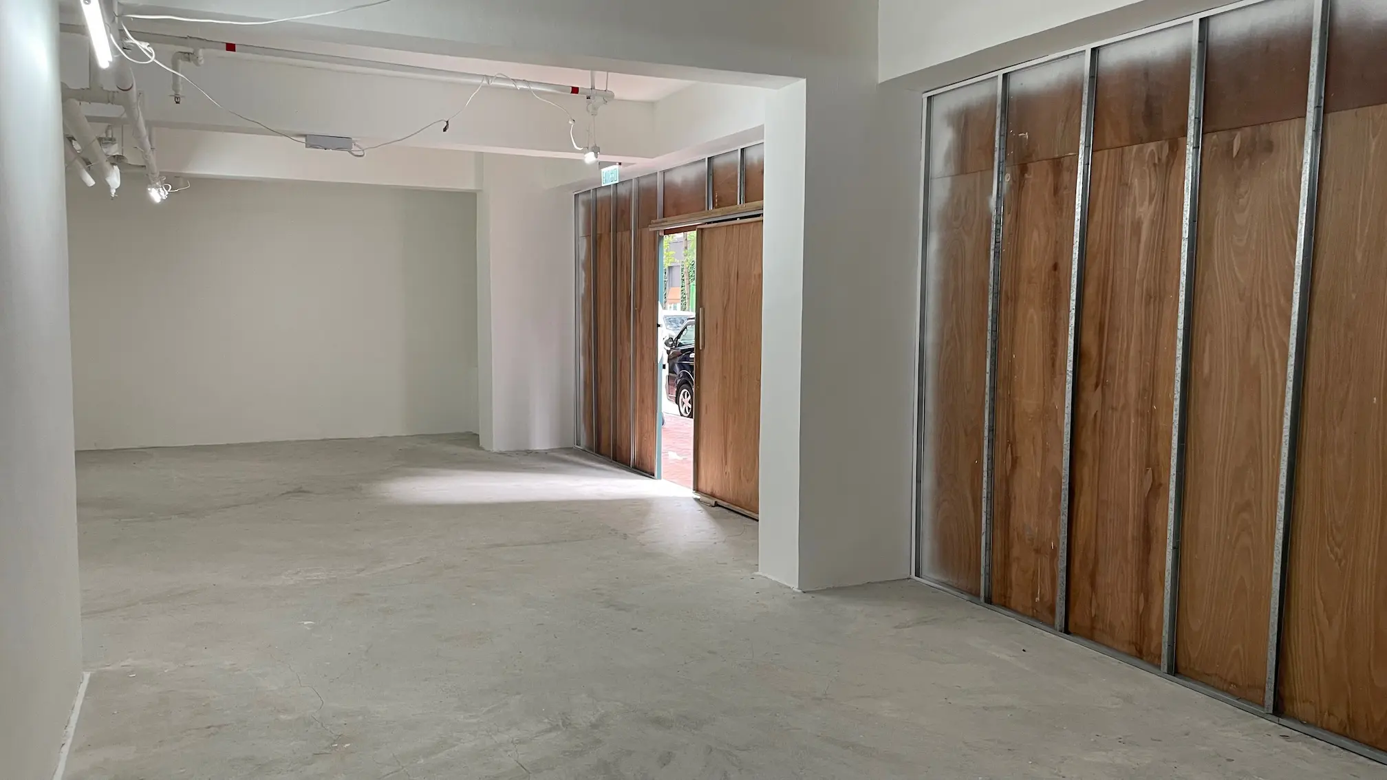 Empty room with concrete floor, white walls, and two large wooden sliding doors opening to Queen’s Road East in Wan Chai.