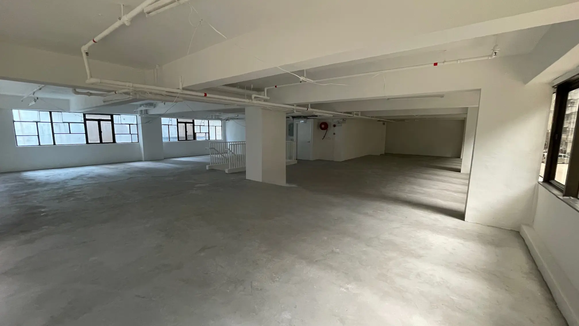 Empty unfurnished room on Queen’s Road East in Wan Chai with concrete floor white walls and exposed ceiling pipes.