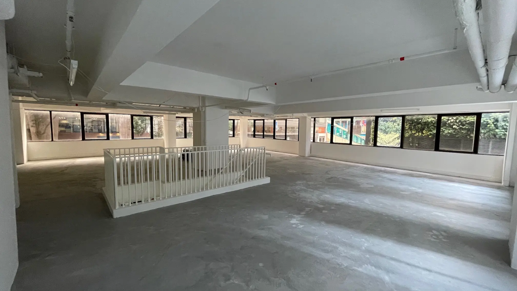 Spacious empty room on Queen’s Road East with large windows, concrete floor, white pillars, and a white fenced section.