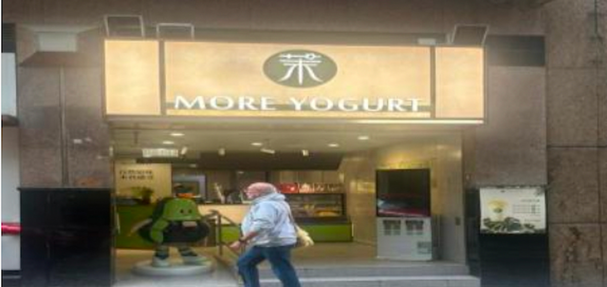 A person walks by the More Yogurt storefront on Stanley Street, Central, with a green mascot standing at the entrance.
