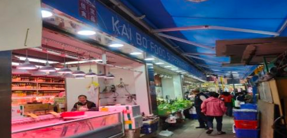 People shop for fresh produce at Wan Chai indoor market under a blue awning on Spring Garden Lane.