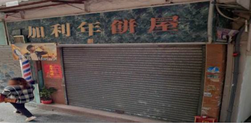 Shop on First Street, Sai Ying Pun. Closed storefront with metal shutter; person with a bag walks past on the left.