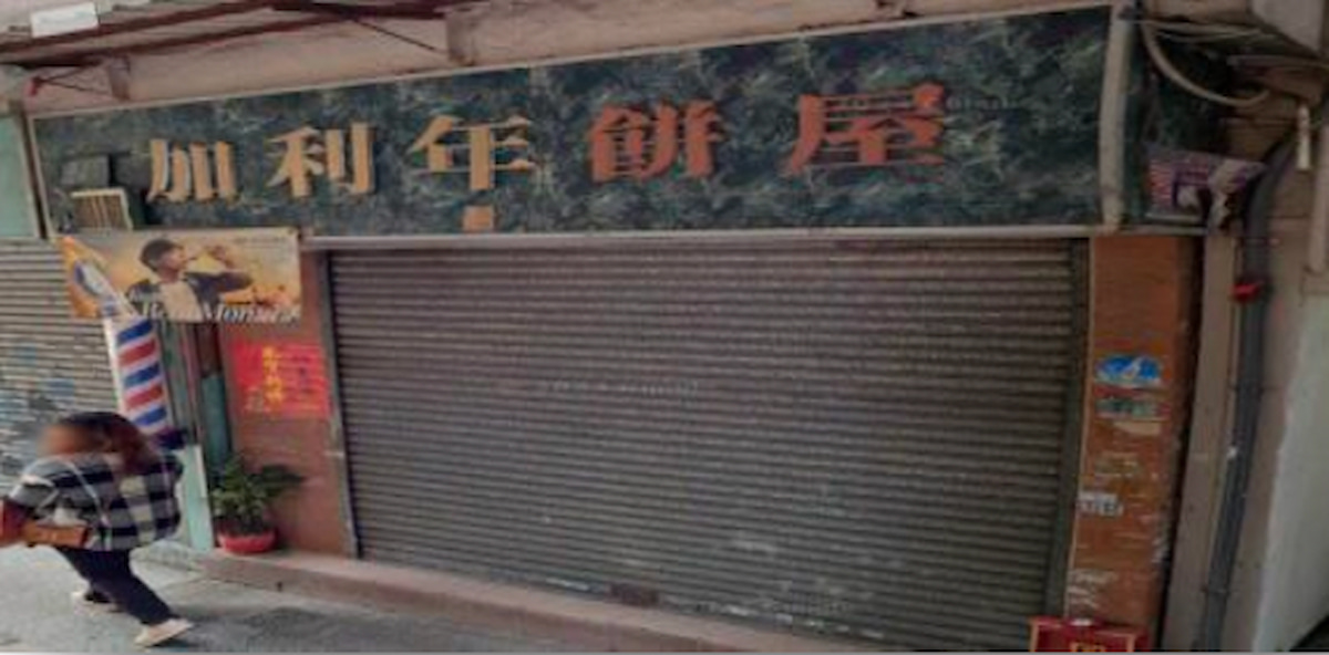 A closed storefront with a metal shutter on First Street, Sai Ying Pun as a person carrying a bag walks past.