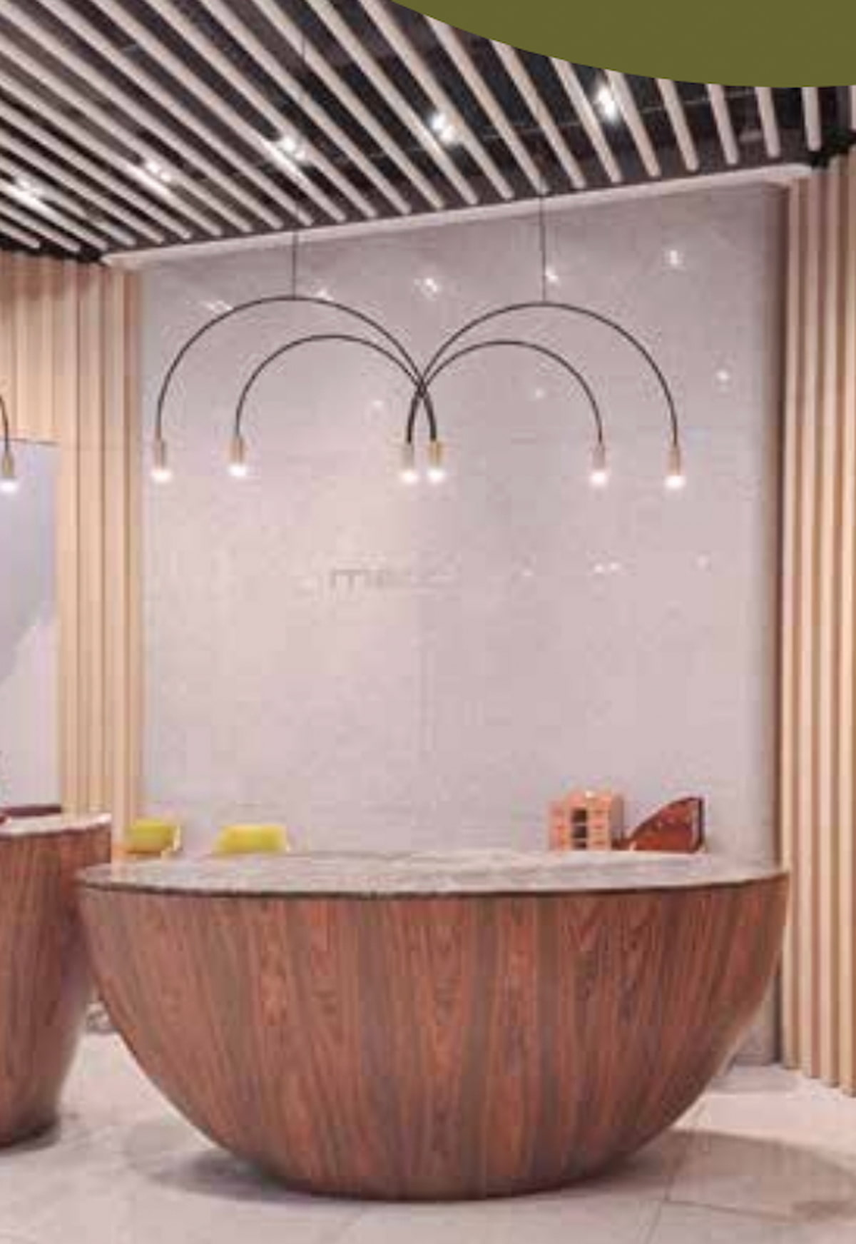 Semicircular wood reception desk with pendant lights in front of a light wall featuring vertical paneling.