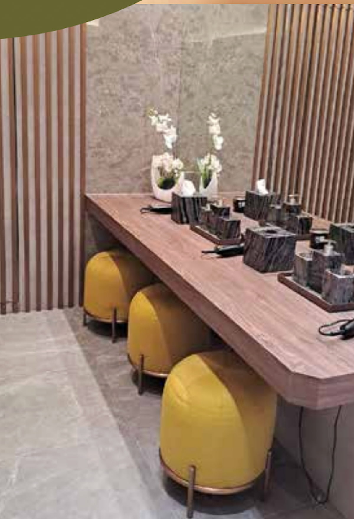 Wooden counter with yellow stools, marble accessories, and white orchids in a modern restroom at Jordan MTR.