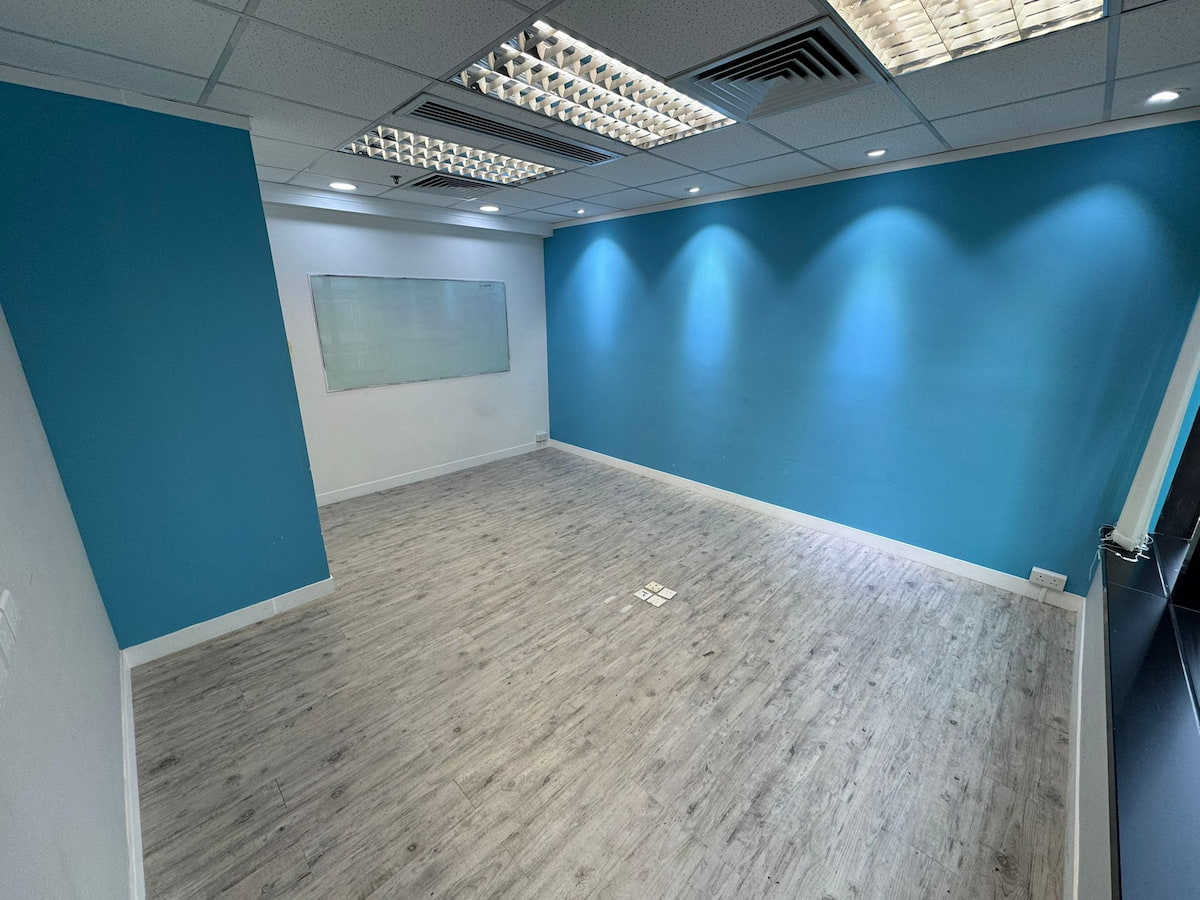 Empty office room on Leighton Road, Causeway Bay with blue accent wall, whiteboard, and gray wood flooring visible.