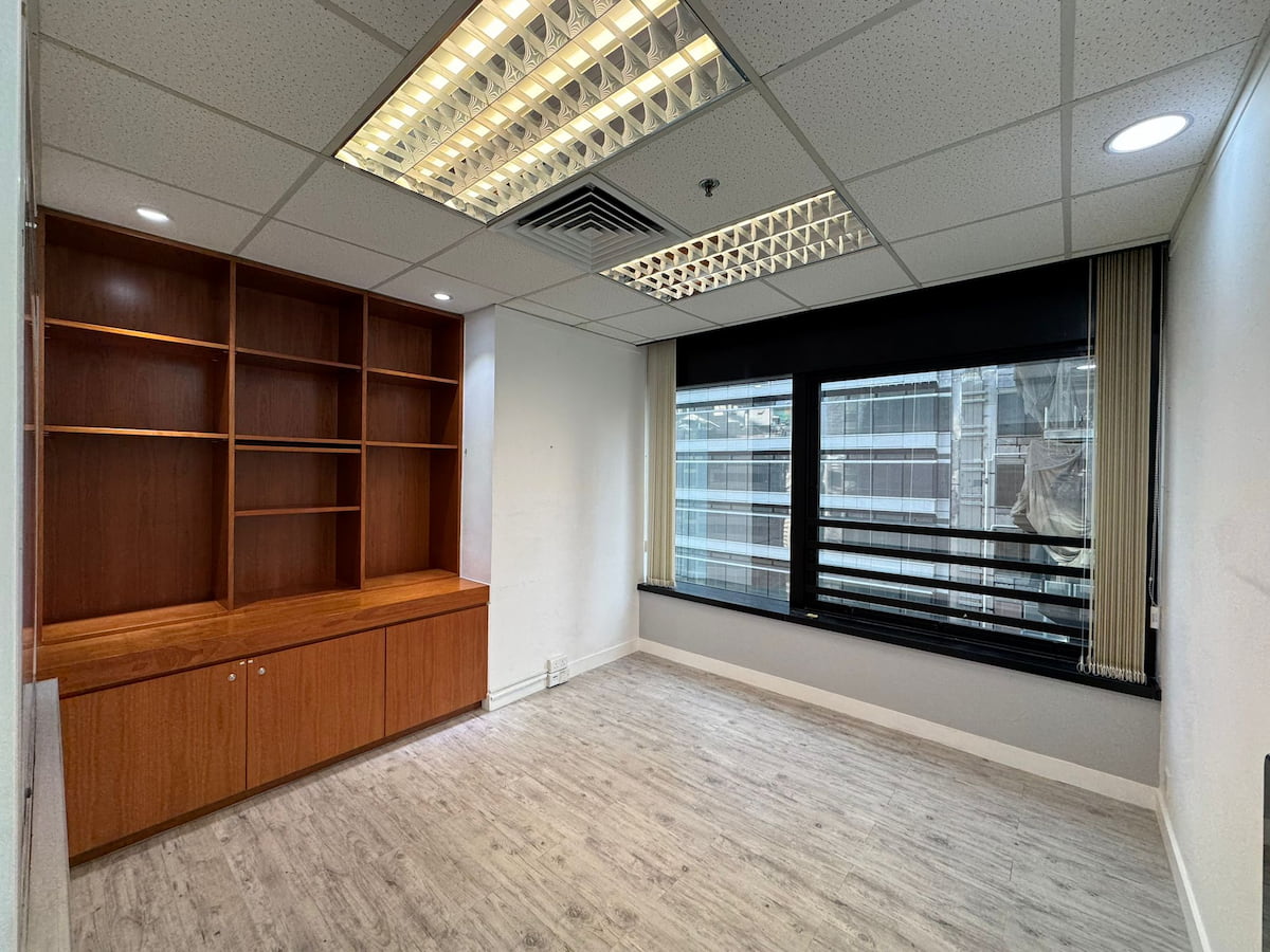 Empty office on Leighton Road with wooden shelves, large window blinds, light wood floor, and white walls.